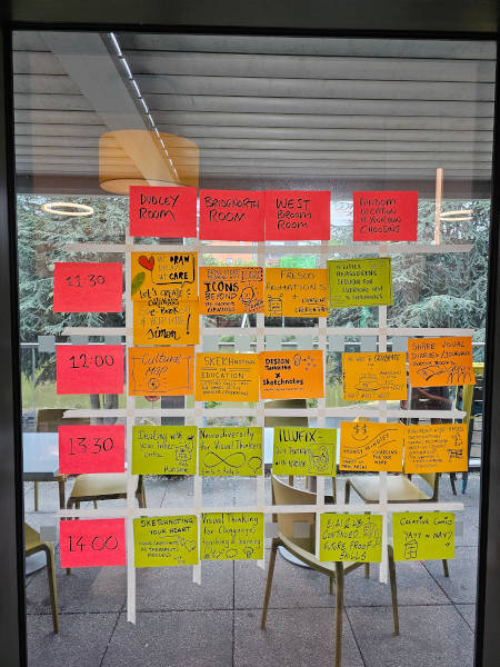 Barcamp day schedule, via a post it note grid on a window, grid cells marked via masking tape